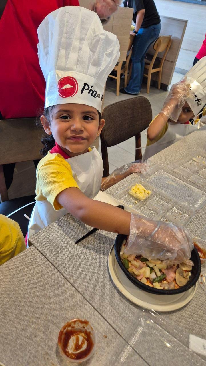 Child in a chef hat during a pizza-making activity